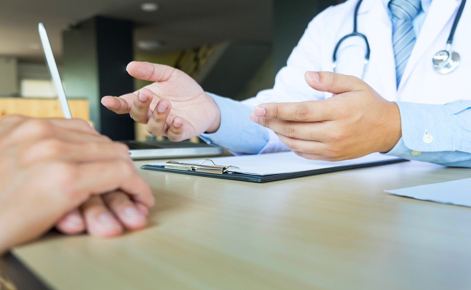 patient listening intently to a male doctor explaining patient symptoms or asking a question as they discuss paperwork together in a consultation.